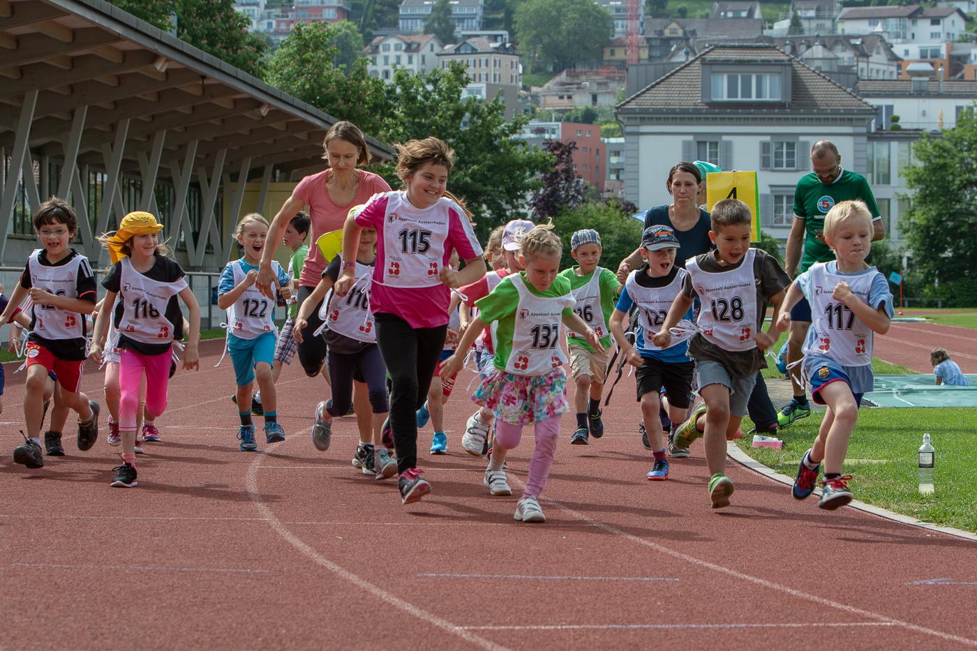 Schüler Basisstufe beim Laufstart mit Startnummern auf Laufbahn